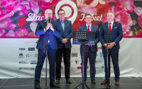 Powiększ zdjęcie: Przemawia prezes Janusz Malinowski, z tyłu stoi trzech mężczyzn na tle banneru z logo Stacja Kobiet