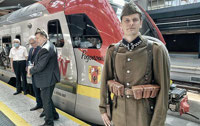 Powiększ zdjęcie: Aktor odgrywający żołnierza z 1920 roku na tle pociągu.