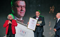 Powiększ zdjęcie: Jan Kotynia stoi na scenie, w rękach trzyma otrzymany dyplom i statuetkę. 