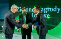 Powiększ zdjęcie: Na scenie Janusz Malinowski odbiera nagrodę, ściska dłoń osobie wręczającej.