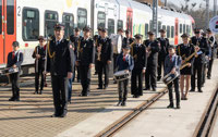 Powiększ zdjęcie: Na zdjęciu Orkiestra o kolejowych tradycjach ze Zduńskiej Woli, składa się z wielu muzyków z instrumentami perkusyjnymi i dętymi. Stoją na tle pociągu ŁKA.