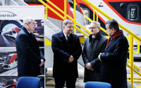 Powiększ zdjęcie: Marszałk i Prezes stoją i rozmawiają, w tle pociąg ŁKA na hali serwisowej. 