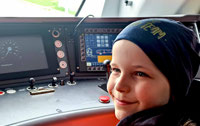 Powiększ zdjęcie: Zdjęcie przedstawia uśmiechniętego chłopca w kabinie maszynisty